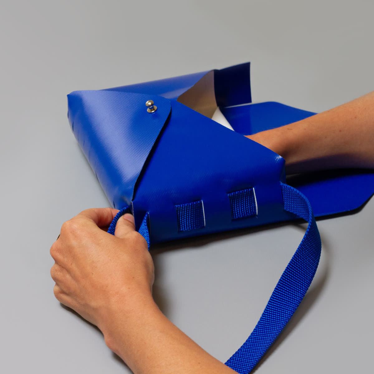 Close-up of hands assembling a Tasket bag, threading the strap